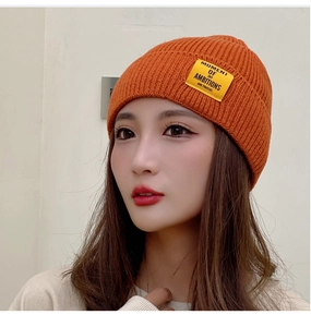 Close-up of orange knitted beanie featuring a yellow text patch and folded brim detail
