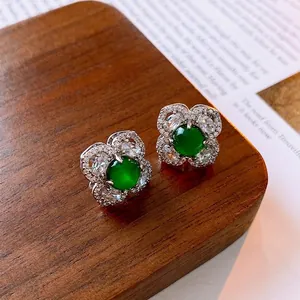 Elegant silver flower earrings with green gemstone and zircon petals on a wood stand