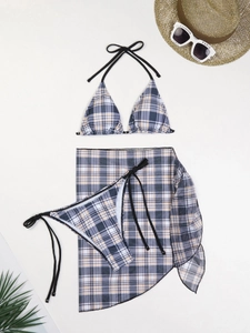 Flat lay of a 3-piece plaid bikini set with sheer wrap skirt, sun hat and palm leaves