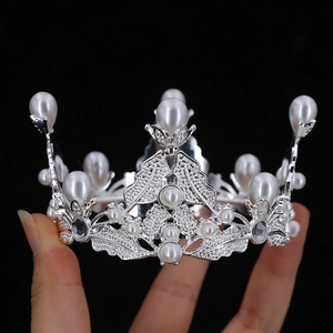 Detail of silver alloy crown featuring white pearls and rhinestones held by hand