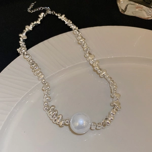 Detailed view of silver crushed bead necklace featuring a white pearl on a ceramic plate