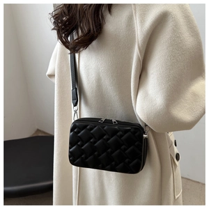 Close-up of a black quilted crossbody bag styled over a white coat with dual zippers