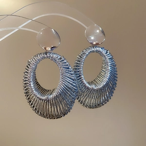 Gros plan d'une boucle d'oreille en fil métallique argenté tissé au design ovale
