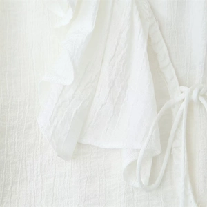 Dettaglio di camicia bianca a pieghe con bordi a balze e design con lacci
