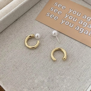Minimalist gold C-shaped hoop earrings with elegant white pearl accents on gray jewelry tray