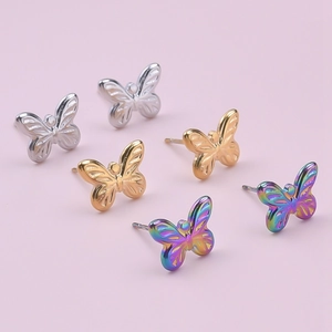 Orecchini a farfalla lucidati in argento, oro e arcobaleno su sfondo rosa chiaro