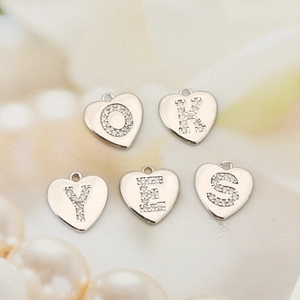 Détail macro de pendentifs en forme de cœur avec zircone montrant les lettres O, K, Y, E, S