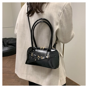 Model wearing a black glossy crossbody bag with gold hardware and top handles