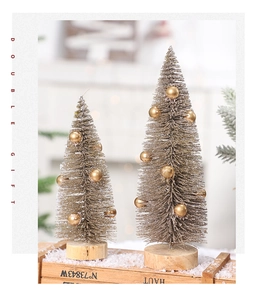 Detail of two champagne gold pine needle Christmas trees with wood bases on snowy wood