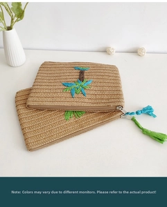 Detail of hand-woven straw envelope clutch bag with tropical leaf embroidery and tassel