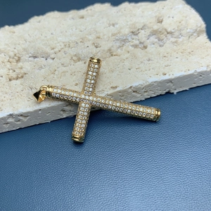 Macro shot of gold plated cross pendant with sparkling zircons on a textured stone