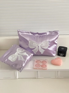 Close-up of purple satin makeup bag set featuring delicate white bow embroidery