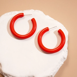 Gros plan de boucles d'oreilles créoles en C rouge vif sur pierre blanche