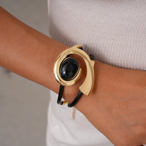 Close-up of golden spiral metal bracelet with a large oval black gemstone on wrist