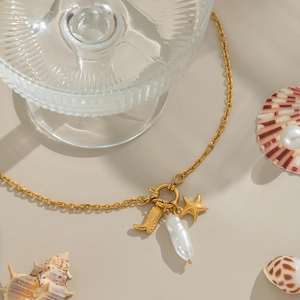 Golden starfish and cowboy boot pendant necklace with baroque pearl on beige backdrop