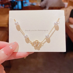 Close-up of gold camellia flower pendant with zircon inlay and pearls on a fine chain