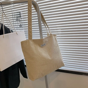 Detail of beige corduroy tote bag with Fashion label hanging against window blinds