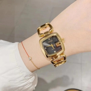 Detail of a gold square watch with black dial and hollow link bracelet on a wrist