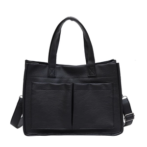 Minimalist black tote bag with textured leather, front pockets and adjustable strap