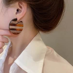 Close-up of model wearing large striped wooden earrings with a retro luxury aesthetic