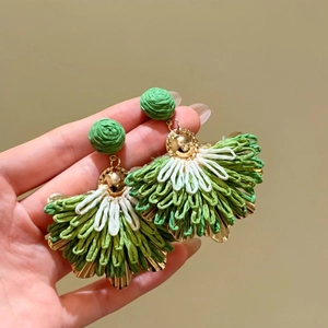 Close-up detailed view of fan-shaped raffia drop earrings with green and white woven design