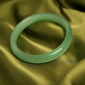 Close-up of polished green cat-eye stone bangle on elegant green silk fabric background