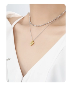Detail of a layered silver bead necklace with a textured golden heart pendant on a model