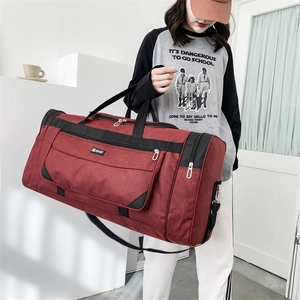 Detail of deep red travel bag with adjustable strap held by model for size scale