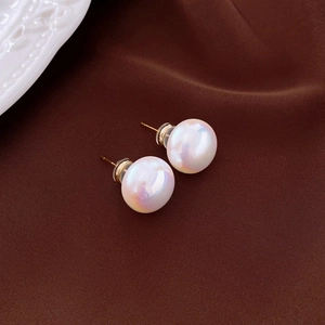 Macro detail of round white pearl stud earrings with golden needles on textured fabric