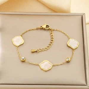 Détail d'un bracelet doré en acier inoxydable avec breloques en émail blanc et zircons