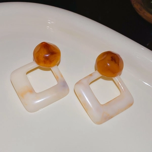 Detailed macro view of geometric resin earrings with amber round top and marbled square base