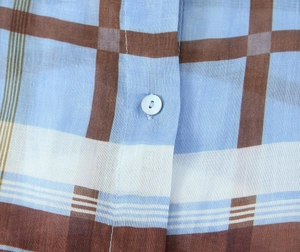 Close-up of light blue and brown plaid ramie fabric with a single round button detail