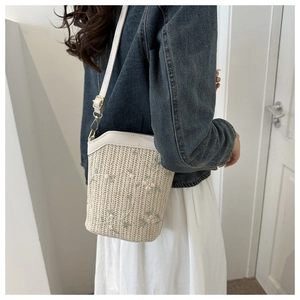Détail d'un sac seau tissé avec broderie florale verte et bandoulière en cuir