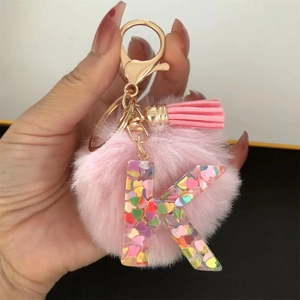 Detail of pink resin letter K keychain with heart glitter, pompom and tassel charm