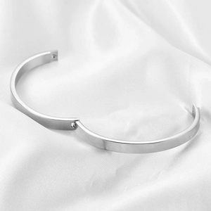 Detail of 6mm polished stainless steel bangle with hinge clasp on white silk fabric