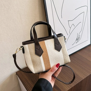 Striped canvas crossbody bag with leather handles shown in a lifestyle hand-held pose