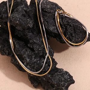 Close-up of gold and silver two-tone flat snake chain set on elegant black stone background