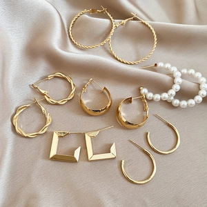 Detail view of assorted gold geometric earrings and white pearls on champagne silk fabric