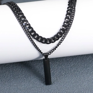 Detail of layered black Cuban chain necklace with rectangular pendant on a white pedestal