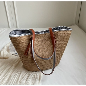 Detail of woven straw tote bag with black and white striped lining and brown tassels
