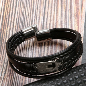 Close-up of black braided leather layers and polished stainless steel clasp on wood