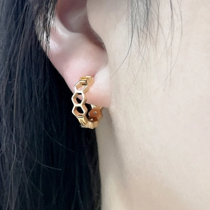 Close-up of gold hexagonal honeycomb earrings with zircons on a model's ear