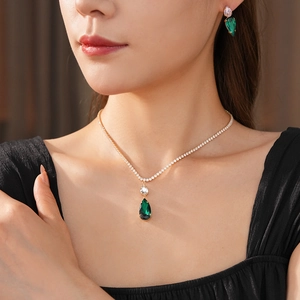 Close-up of model wearing green teardrop emerald pendant necklace and earring set