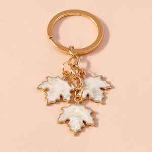 Detailed macro shot of a gold-plated keychain with white enamel ginkgo leaf pendants