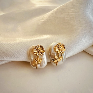 Close-up of golden floral earrings with baroque pearls on soft silk background