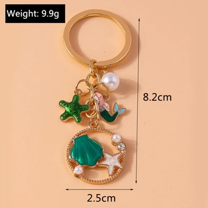Golden keychain with green starfish, mermaid, and shell charms on light orange background