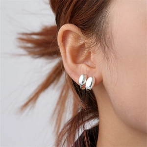 Minimalist silver bean stud earrings with high-polish mirror finish shown on ear