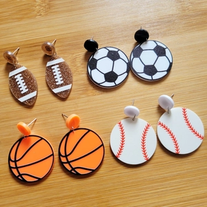 Flat lay of acrylic sports ball earrings featuring football, soccer, basketball and baseball