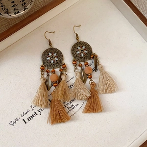 Close-up of bohemian tassel earrings with bronze floral disks and beige fringes