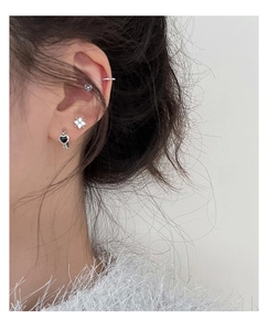 Close-up of small silver heart earring, flower stud and ear cuff on a female ear
